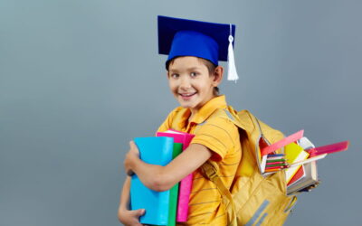 Jeune garçon souriant portant un bonnet de diplômé et un sac à dos rempli de fournitures scolaires pour la rentrée.