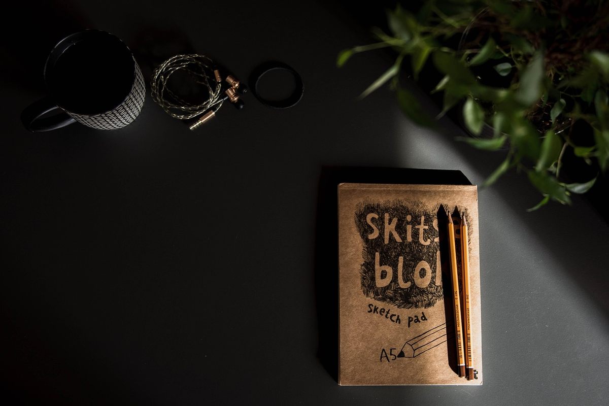 Un cahier, deux crayons, une tasse, une plante et des accessoires sur table sombre