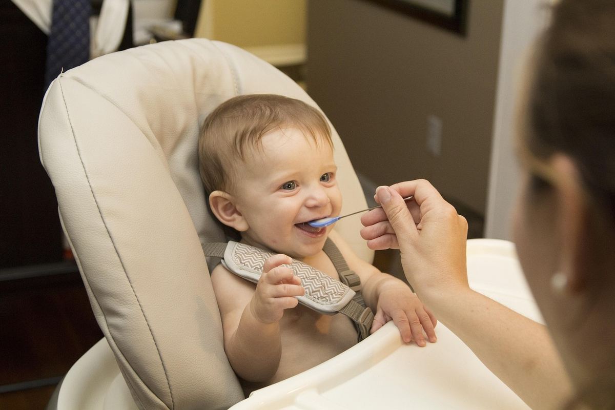 Un bébé souriant mange une bouchée avec une cuillère