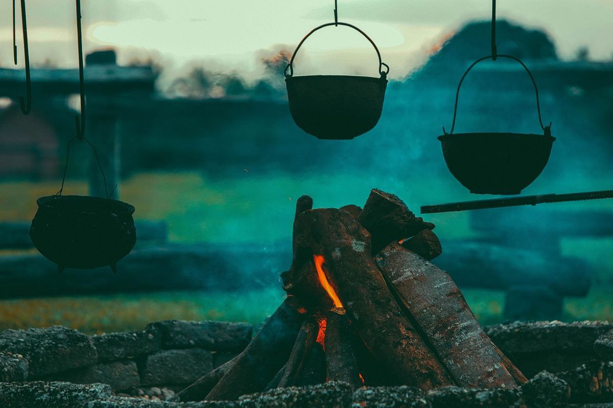 Feu de camp avec trois casseroles suspendues en pierre et bois