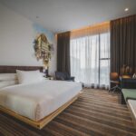 Une chambre moderne avec lit king, canapé vert, bureau et vue grande fenêtre
