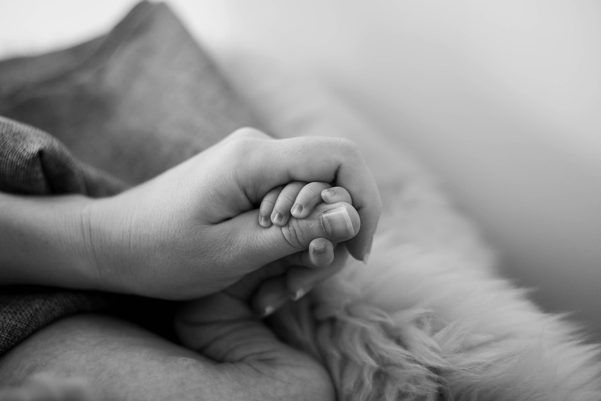 Une main adulte serre doucement une petite main sur un tissu moelleux