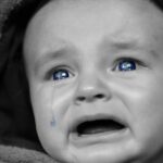 Un bébé en capuche pleure, une larme coule, ses yeux sont bleus