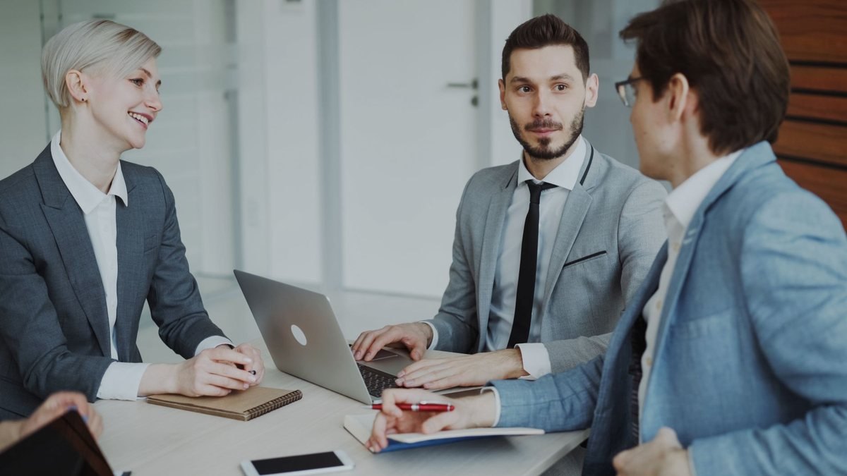 Trois personnes en costume discutent autour d'une table avec ordinateur portable