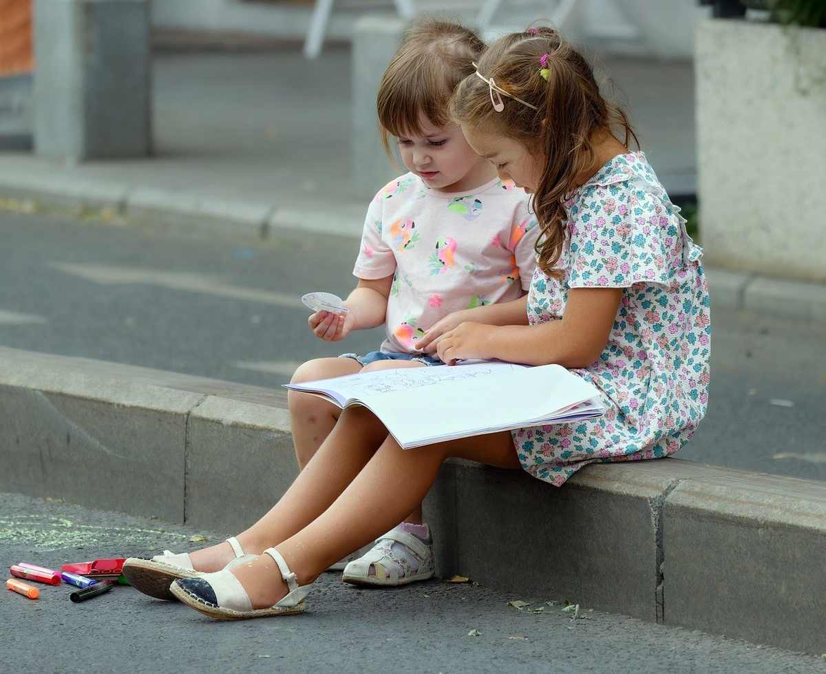 Filles lisant un livre à l'extérieur avec des crayons de couleur à proximité