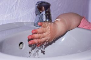 Petite main d'enfant en rose se lavant sous un robinet dans un lavabo blanc