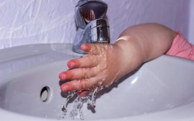 Petite main d'enfant en rose se lavant sous un robinet dans un lavabo blanc