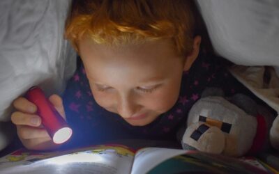 Enfant sous couette, lampe torche éclaire un livre ouvert