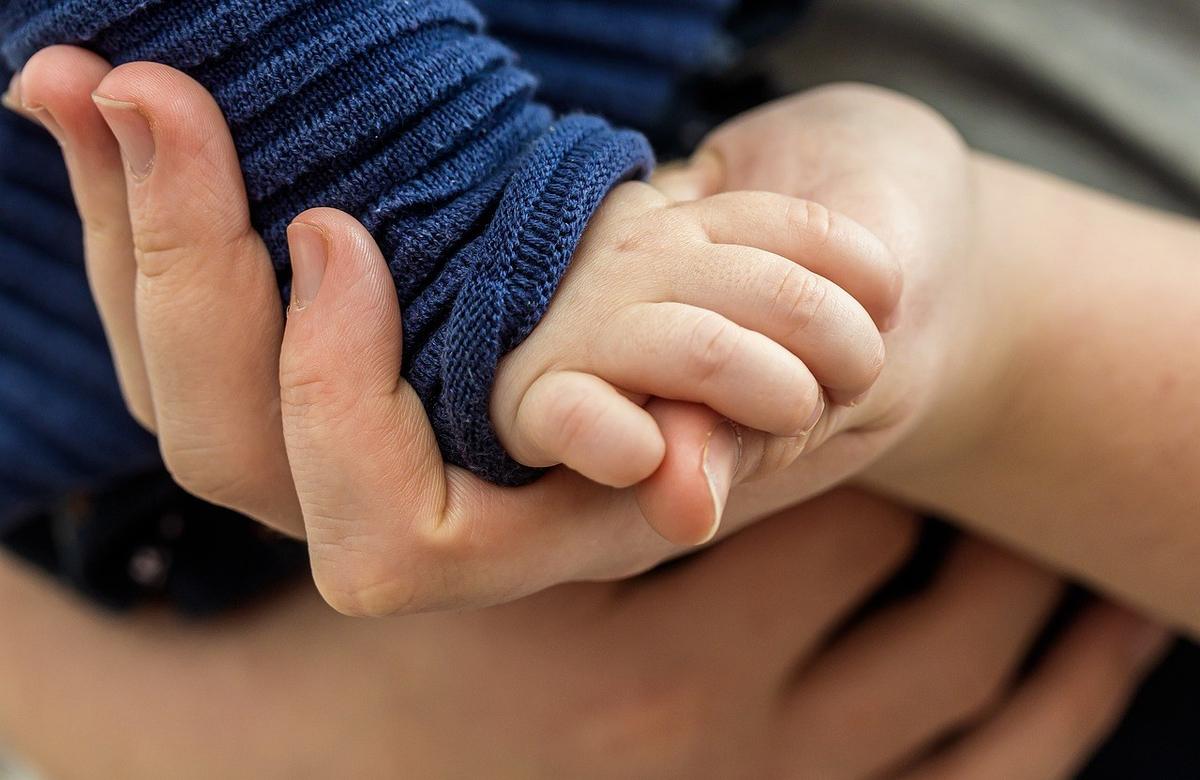 Mains d'adulte et d'enfant se tenant la main, pull bleu et vêtement gris