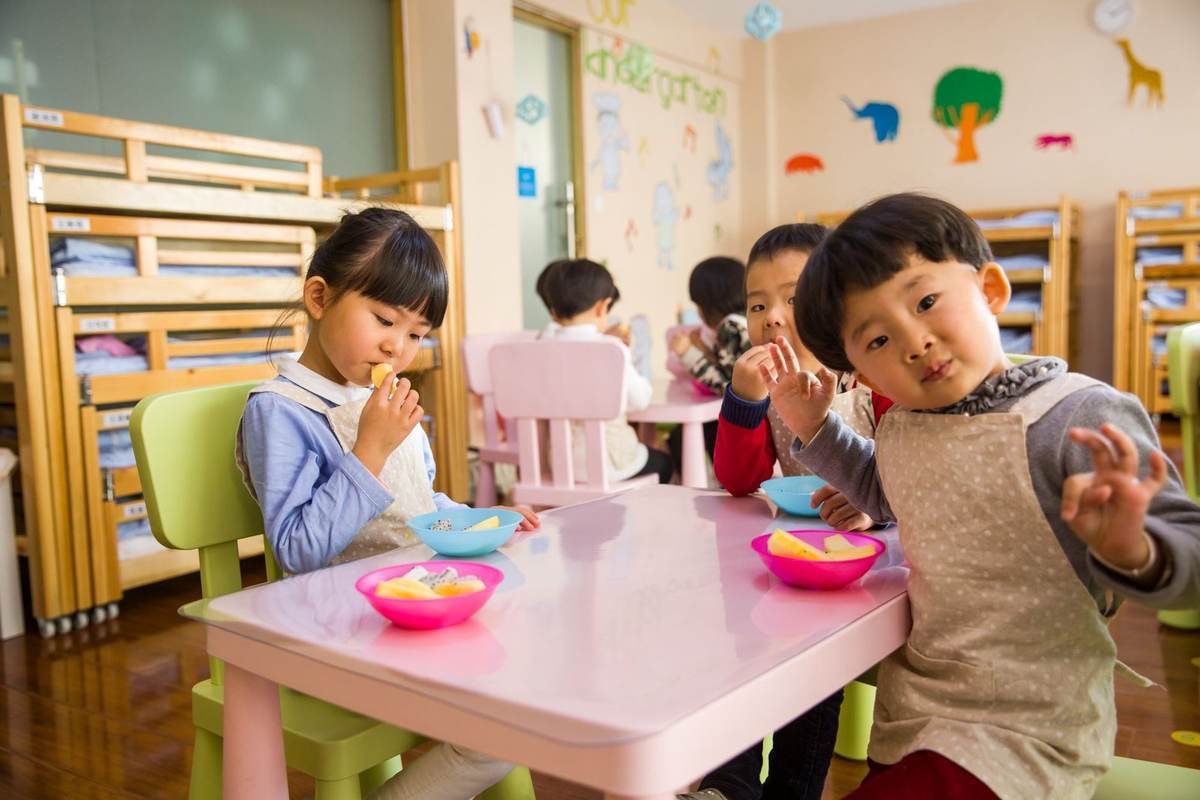 Enfants assis autour d'une table, mangeant, dans une salle de classe